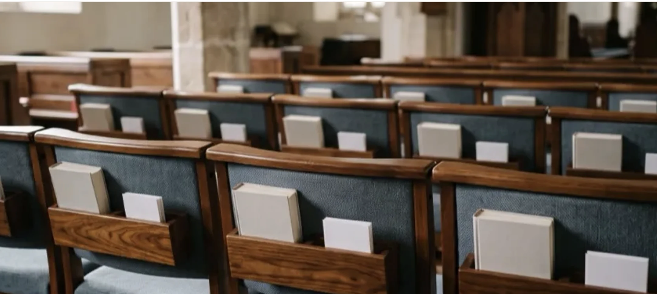 Rear wooden book racks holding hymnals and cards on upholstered wood-frame church chairs